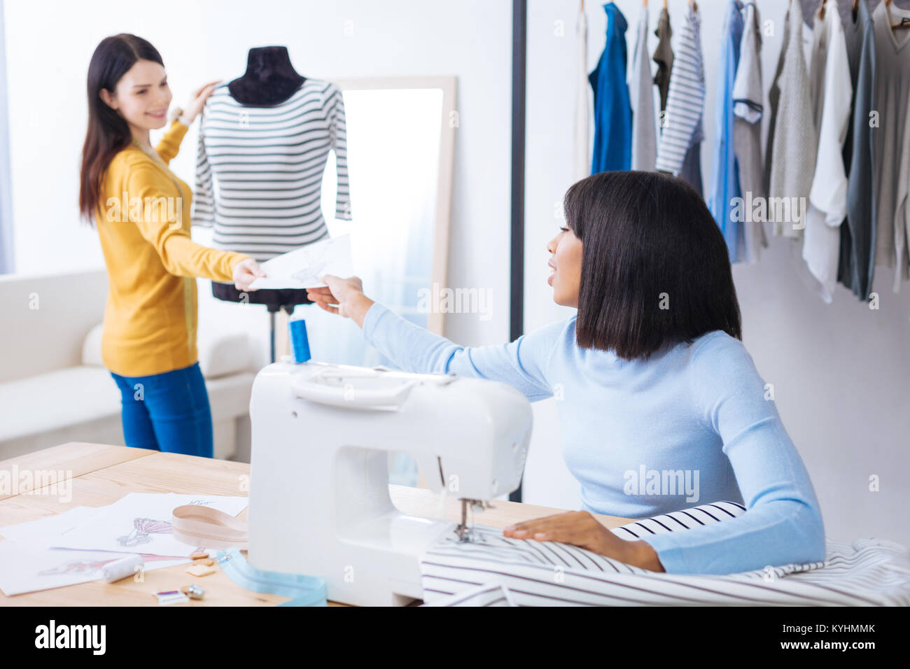 Friendly tailor giving a sketch to her cheerful colleague Stock Photo ...