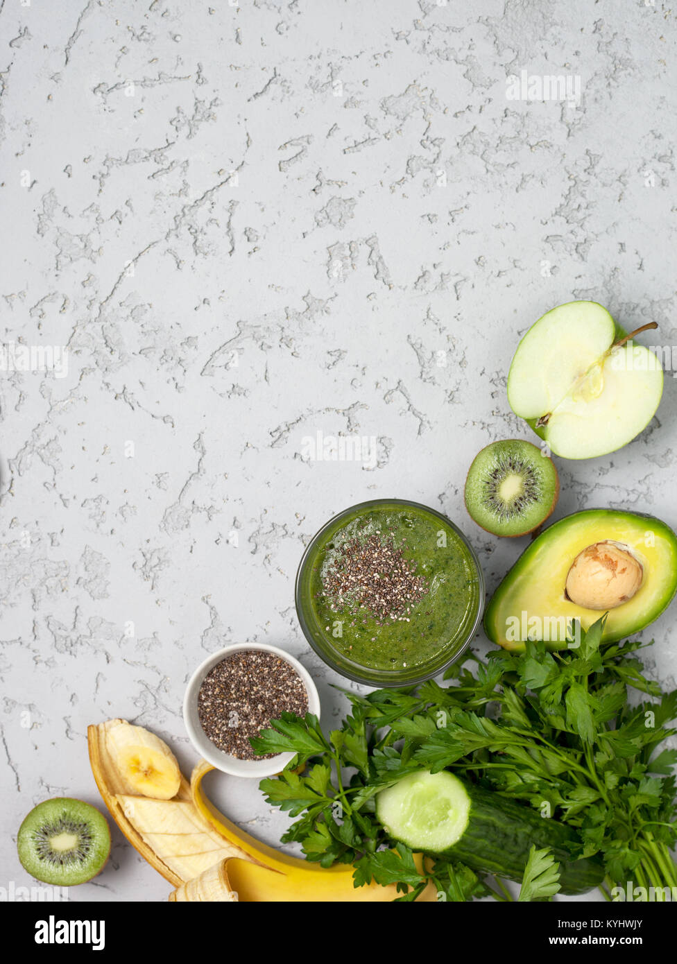 green smoothies in a glass, fresh vegetables, fruits, herbs on a gray concrete background. view from above Stock Photo