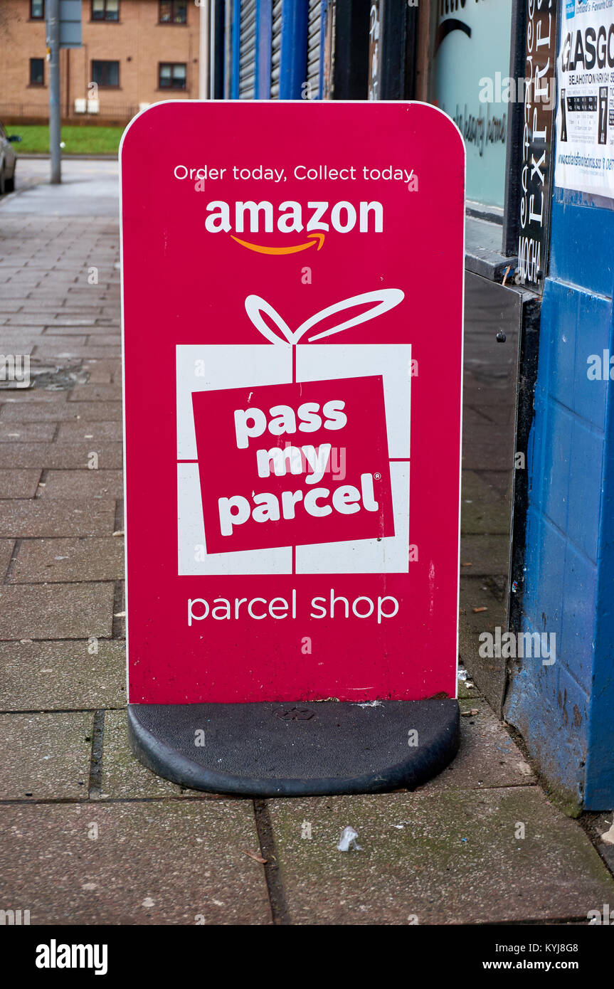 Amazon pass my parcel pink banner ad in front of a local newsagent acting as parcel shop. Stock Photo