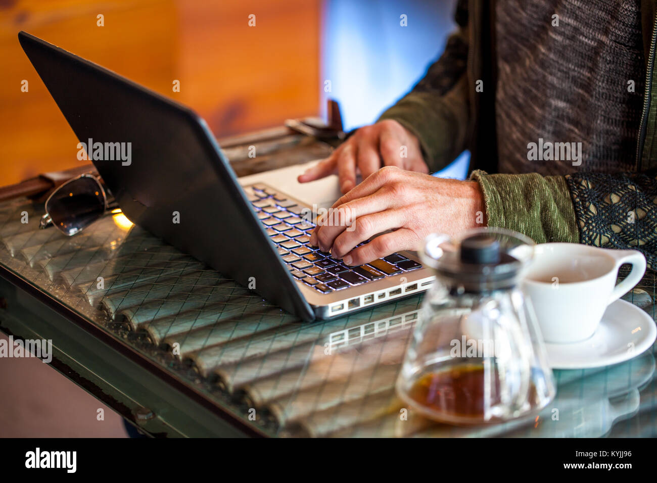 Caucasian man's hands type on laptop  with coffee mug and coffee cup next to him in a coffee shop with focus on keyboard Stock Photo