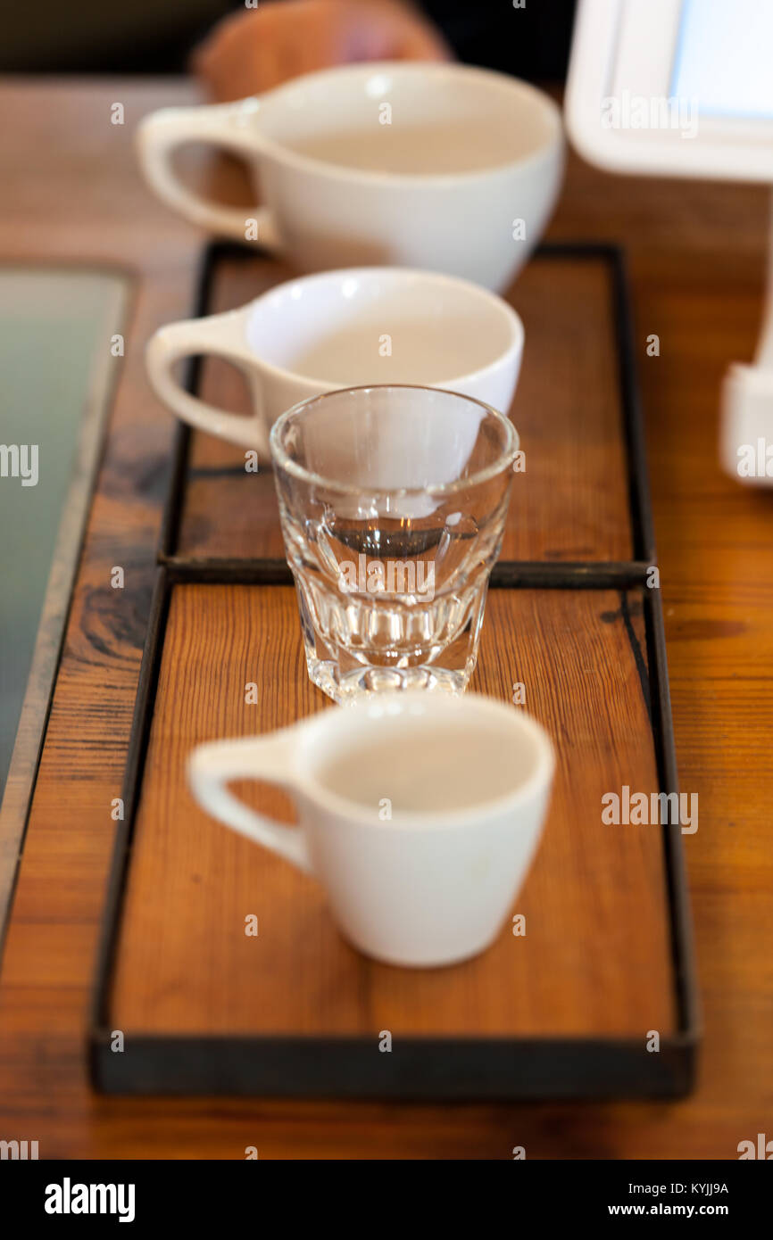 Coffee cups of various sizes next to tablet register in coffee shop on wooden background Stock Photo