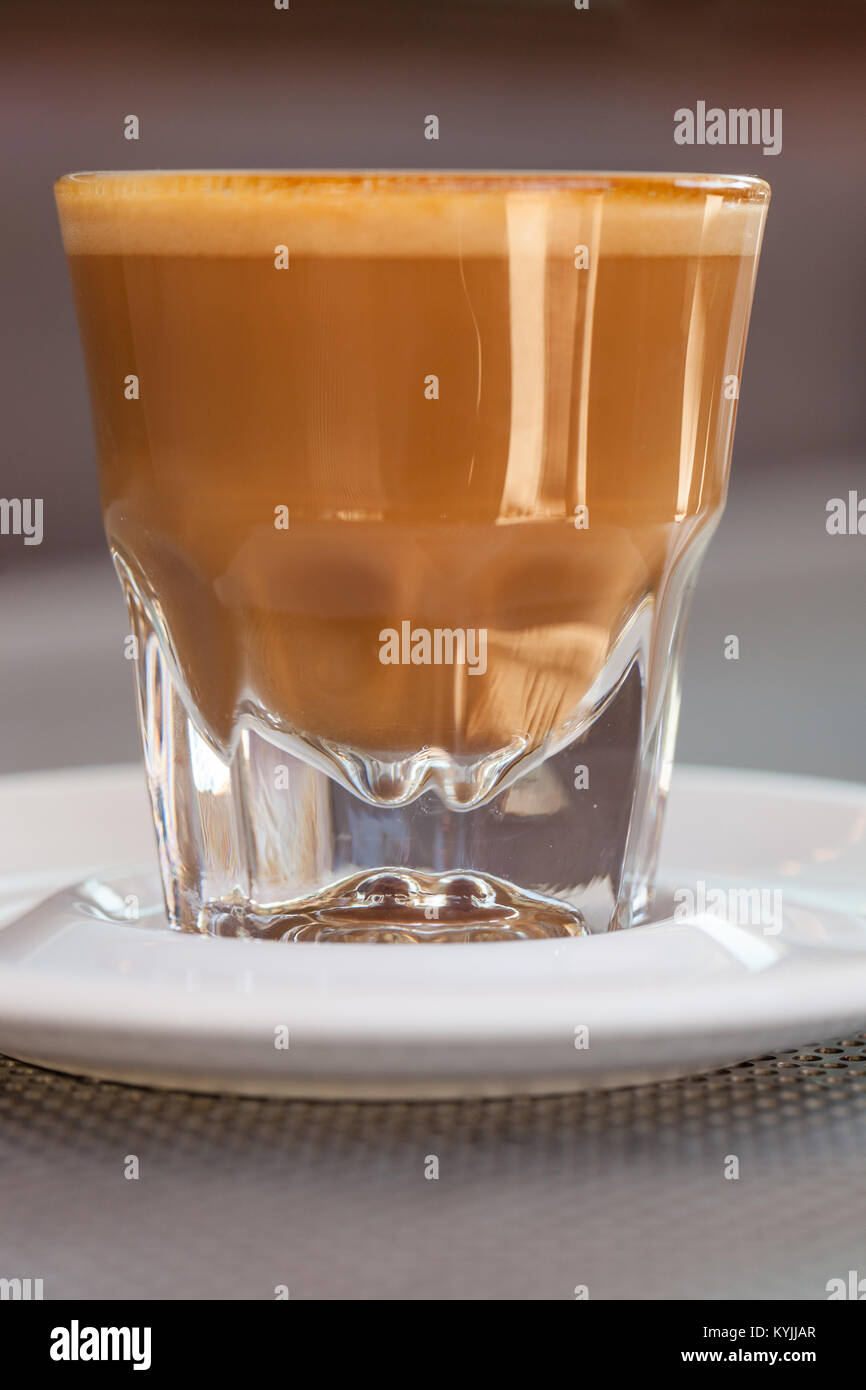Side view of Cortado coffee in a small glass with ceramic saucer on metallic table Stock Photo