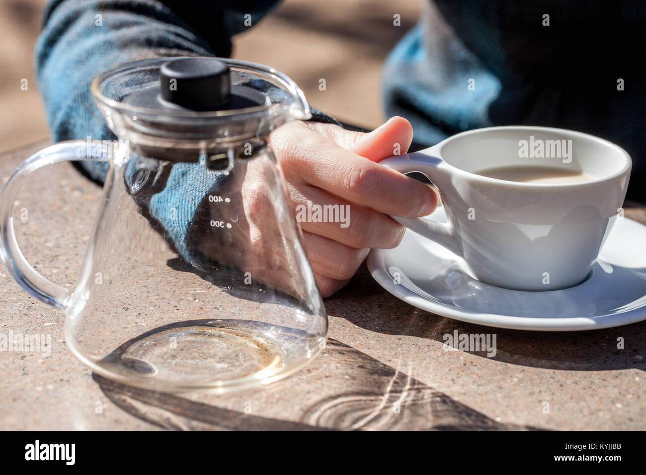 Caucasian woman hand holds ceramic cup with black tea and milk, empty glass teapot next to it Stock Photo