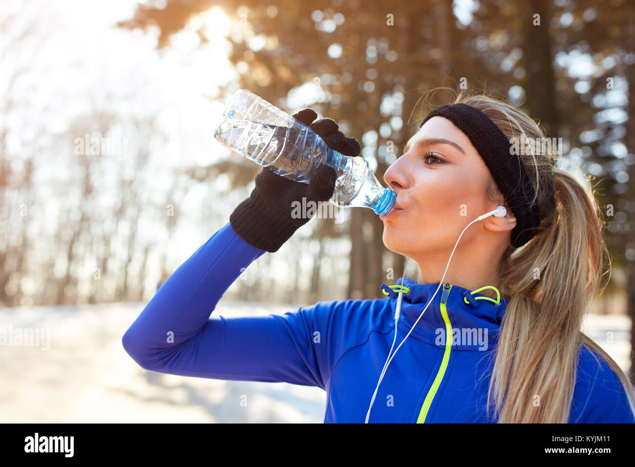 Thirsty female athlete drinking water after running in forest Stock