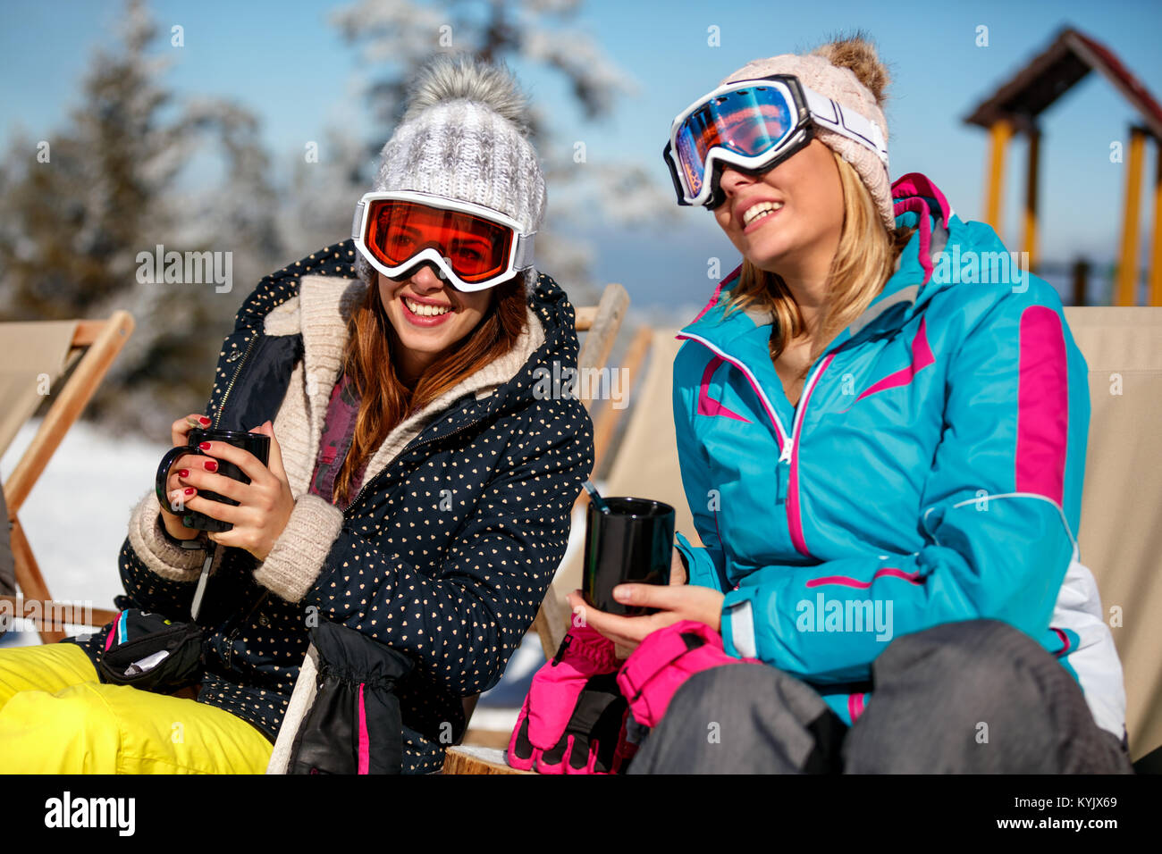 Happy girls friends enjoying hot drink in cafe at ski resort. Sunbathing in snow Stock Photo