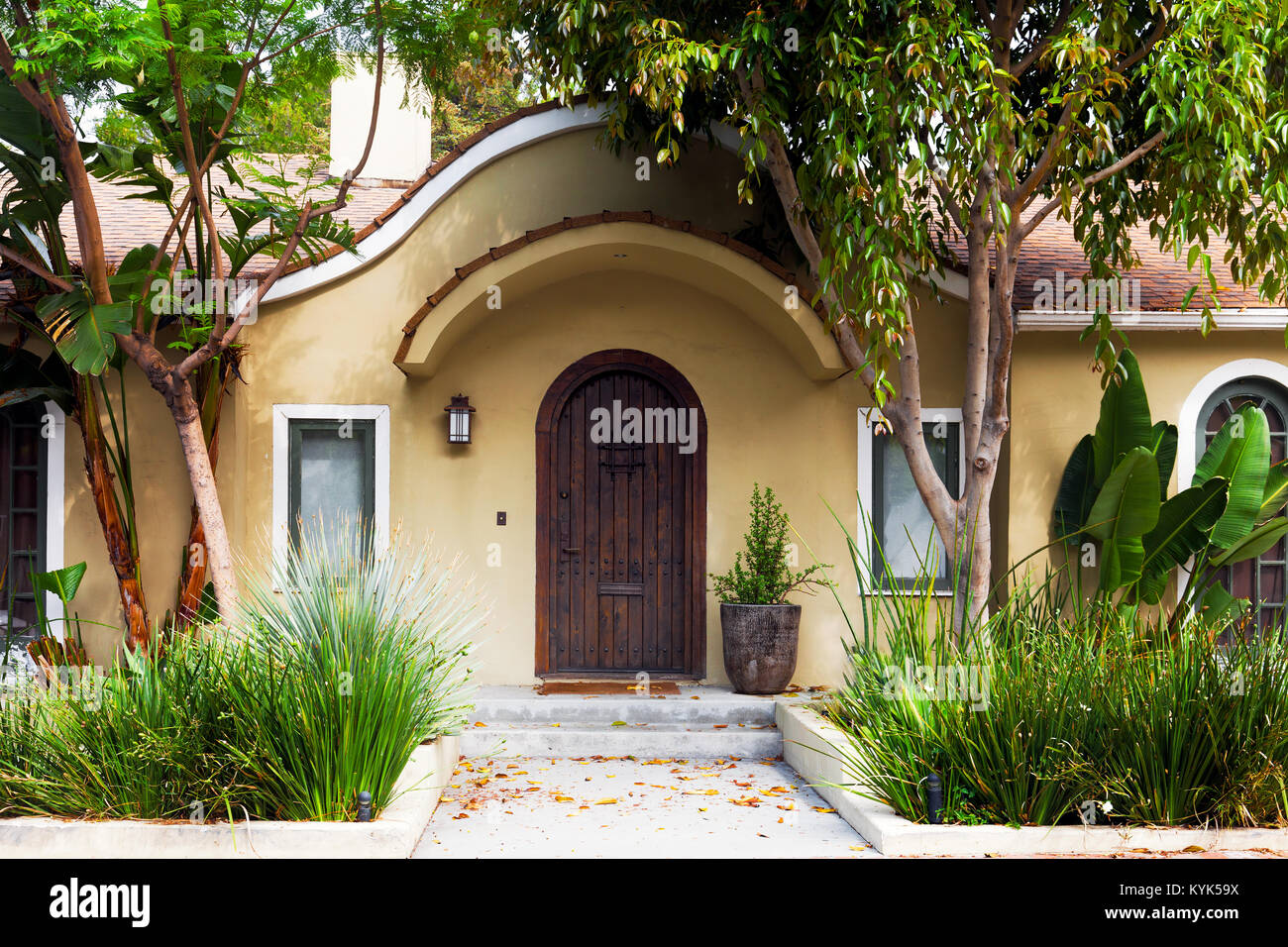 Modern Mediterranean house exterior in Los Angeles. Front door flanked by tropical plants. Arched eyebrow awning Stock Photo
