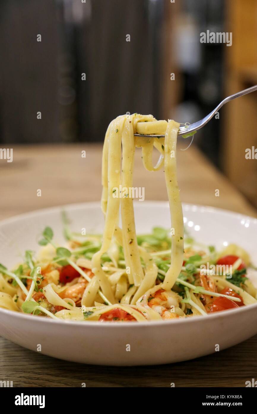 using stainless fork pick pasta / linguine with scrimp scampi in a white dish on a wooden table up Stock Photo