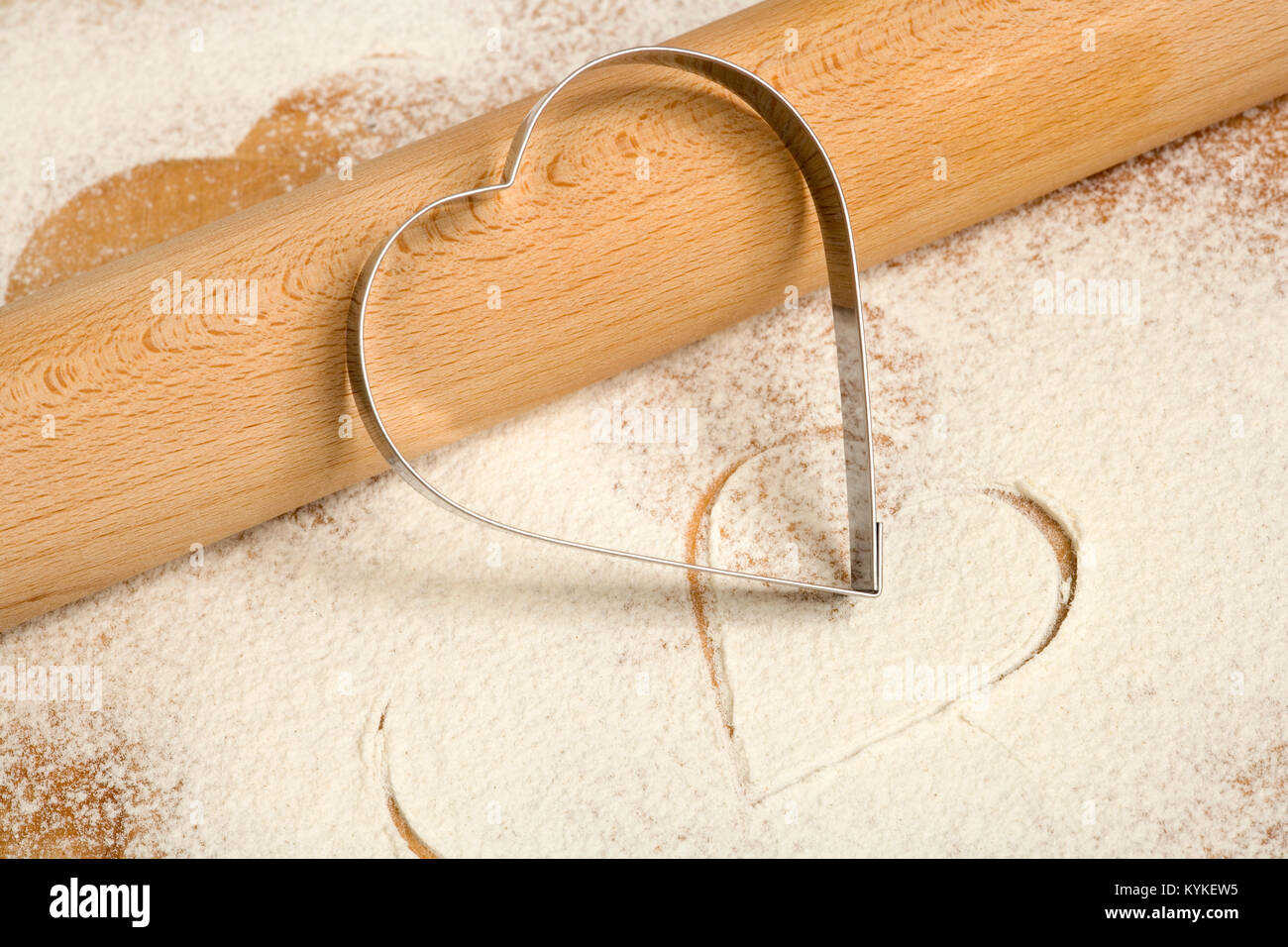 Heart shaped cookie cutter and rolling pin on a a flour dusted worktop