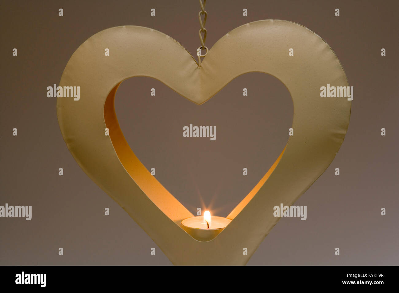 Burning tealight candle in a heart shaped metal candle holder hanging in  front of a graduated plain background Stock Photo - Alamy