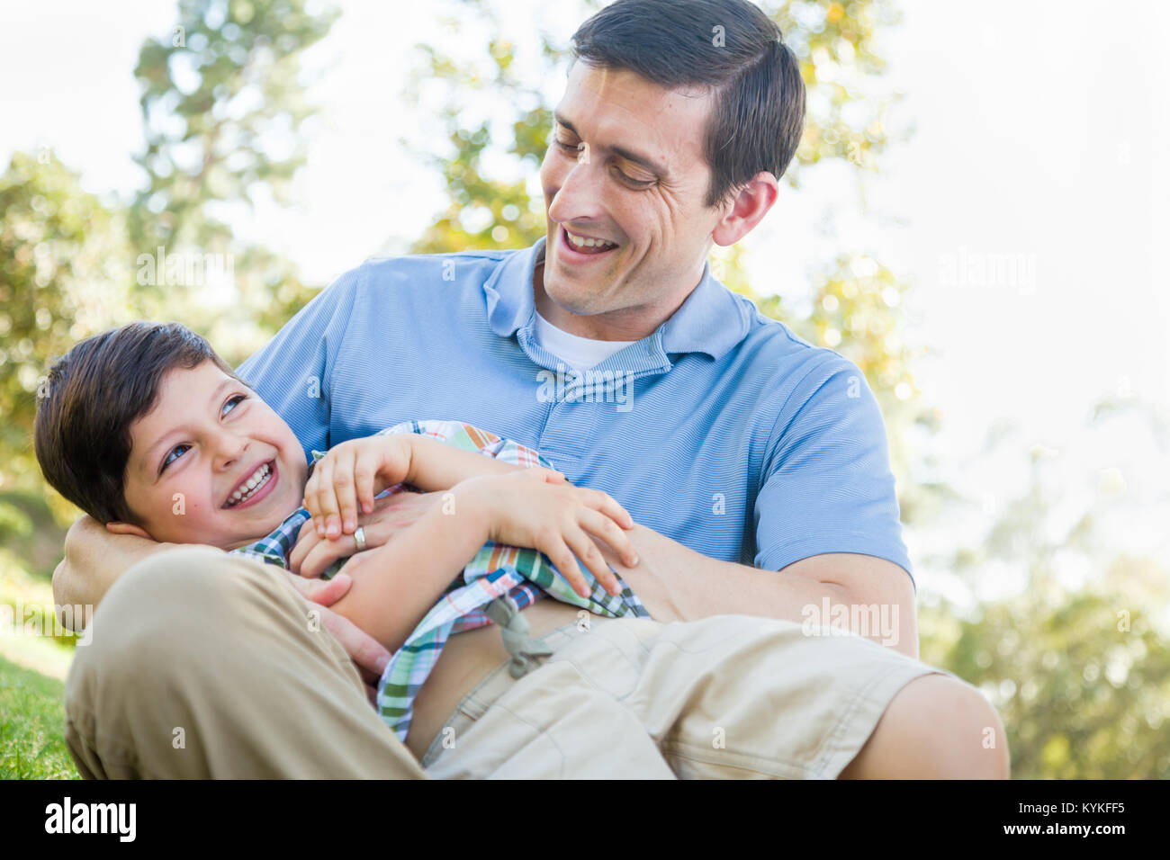 Loving Young Father Tickling Son in the Park. Stock Photo