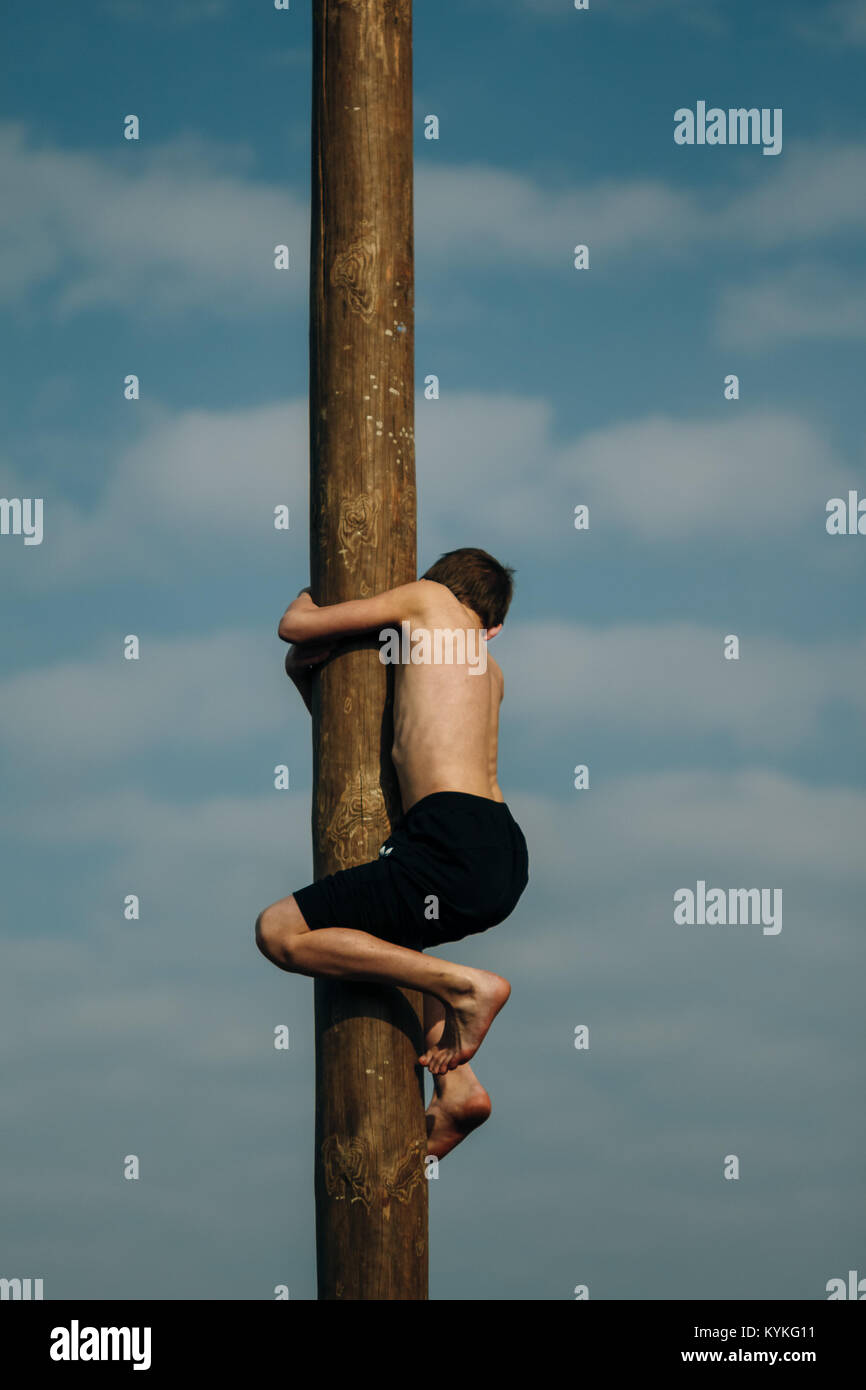 Gomel, Belarus - March 12, 2016: Young boy crawling on a wooden post at the top of the souvenir. People playing the Slav peoples in the celebration Sh Stock Photo