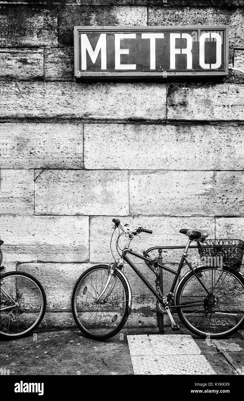 Paris Metro sign above a bicycle parked against a stone block wall. Black and white. Copy space. Gritty graphic style Stock Photo