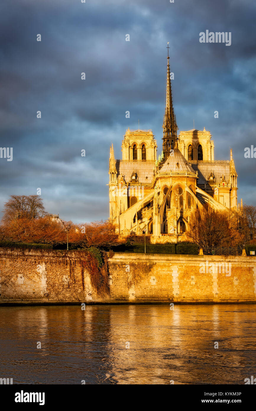 Paris, France Notre Dame Cathedral glowing in golden sunrise dawn light, shining against dark clouds. Reflections in the river below. Dramatic image. Stock Photo