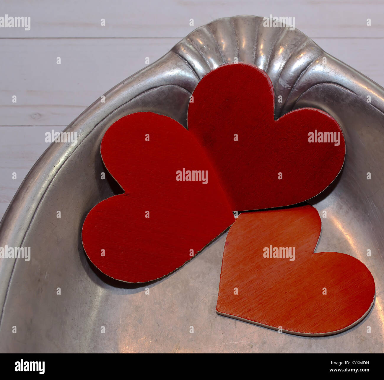 Three red painted hearts laying together in a silver tray on a wooden table Stock Photo