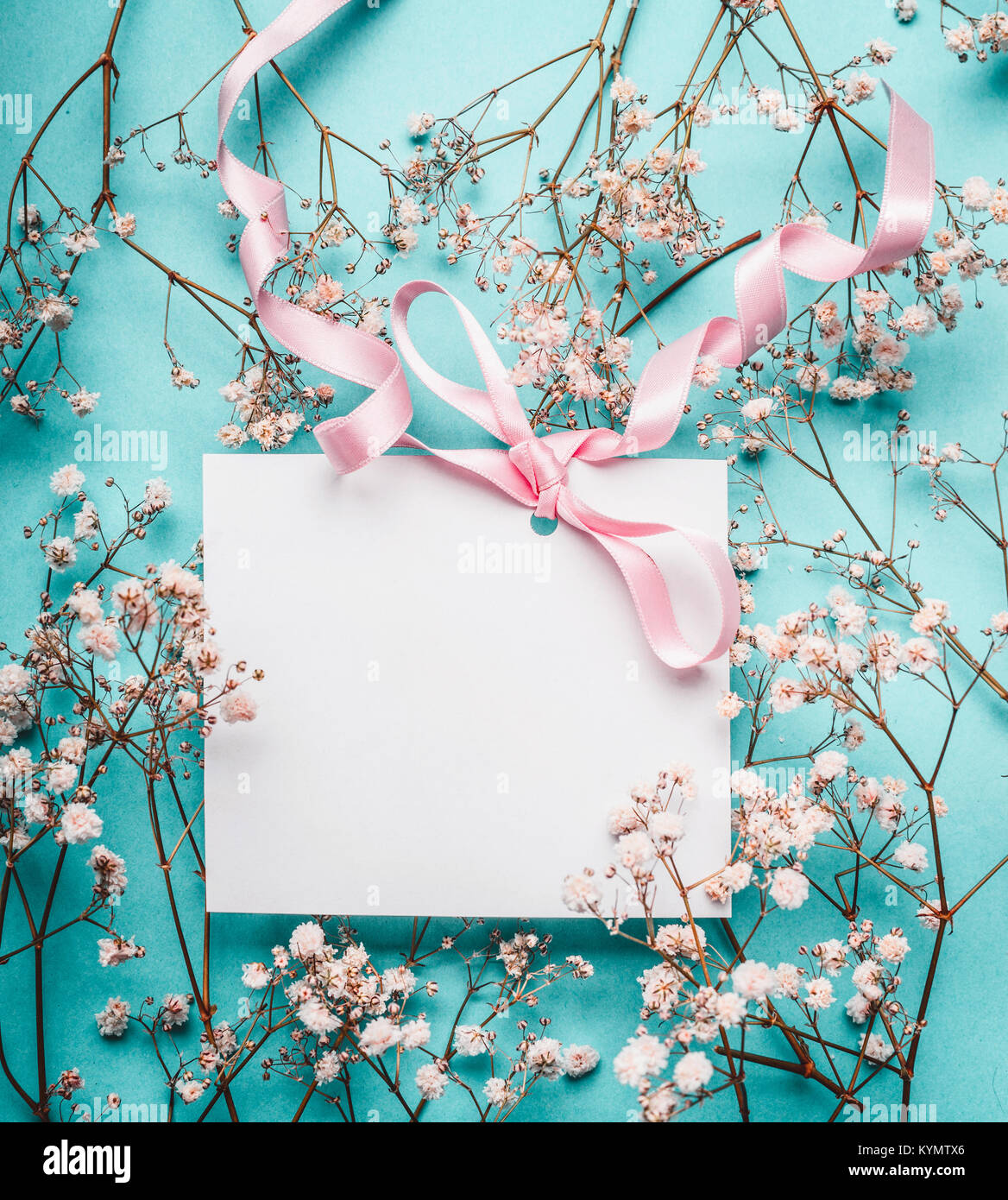Blank white greeting card with pink ribbon on little white flowers at ...