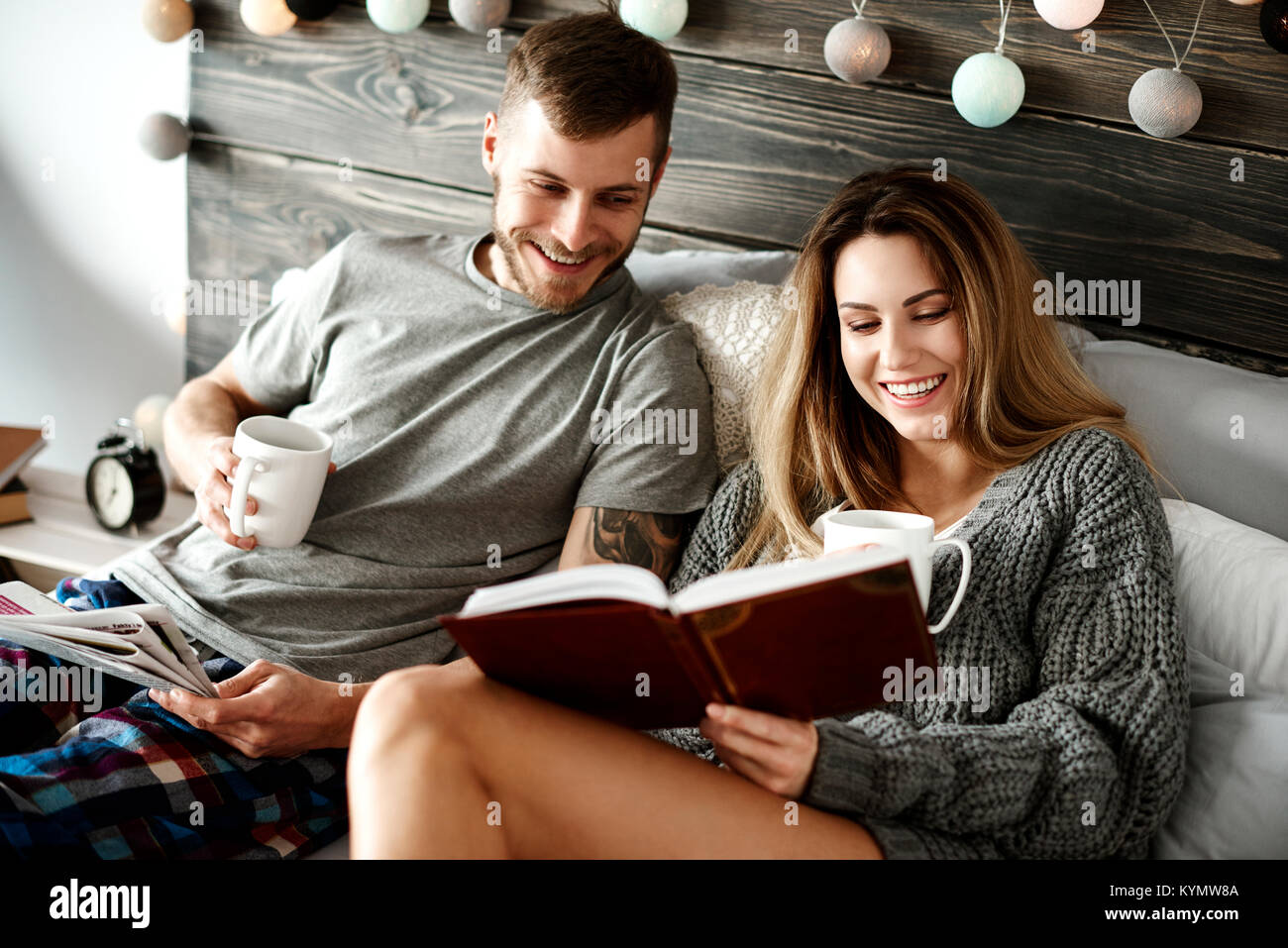 Happy young couple with coffee reading in bed Stock Photo