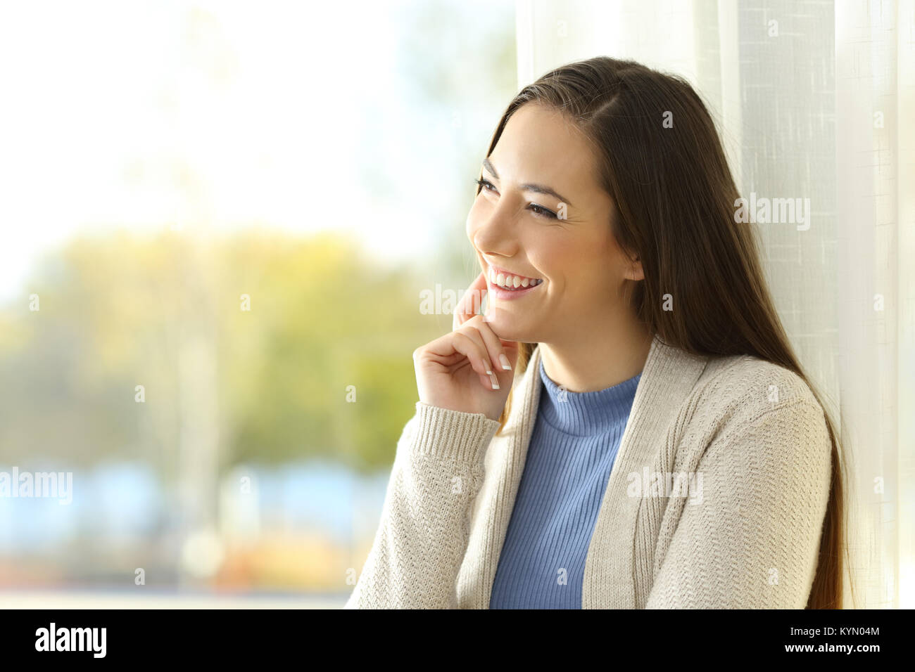 Joyful woman thinking looking at side through a window at home Stock Photo