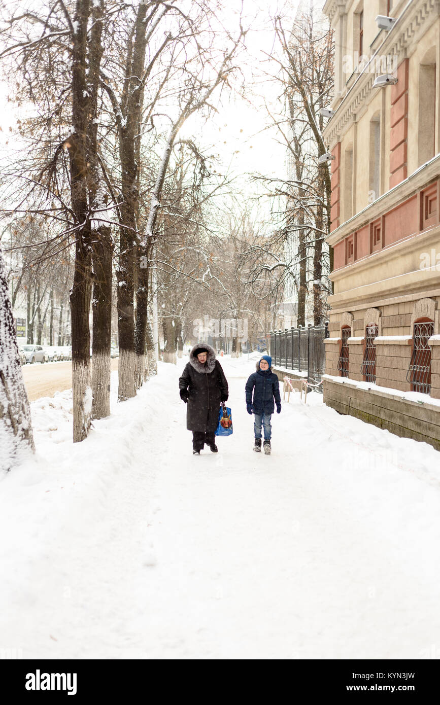 young boy and his grandmother walk down a tree lined snow covered footpath sidewalk in winter in Russia in the city of Ufa in January Stock Photo