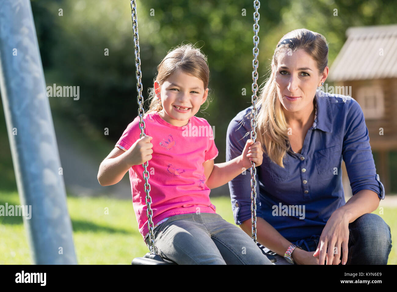 Woman with laughing girl on swing having fun together Stock Photo