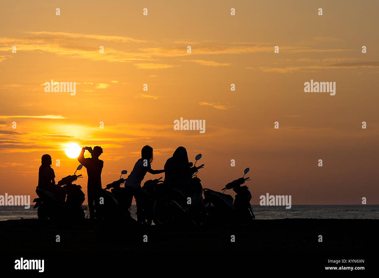 February 2nd 2017 - Padang, Sumatra, Indonesia. Group Gang of Teenagers Young Adults watch a beach side sun set on their scooters. Stock Photo
