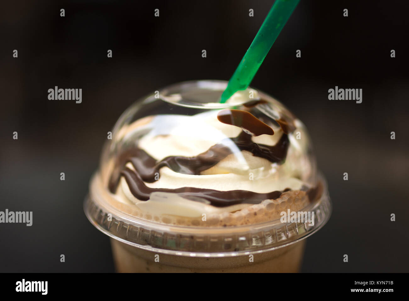 Close up of whipped cream and chocolate sauce on top of a Java Chip Frappe in a clear plastic cup and with a green straw. Stock Photo