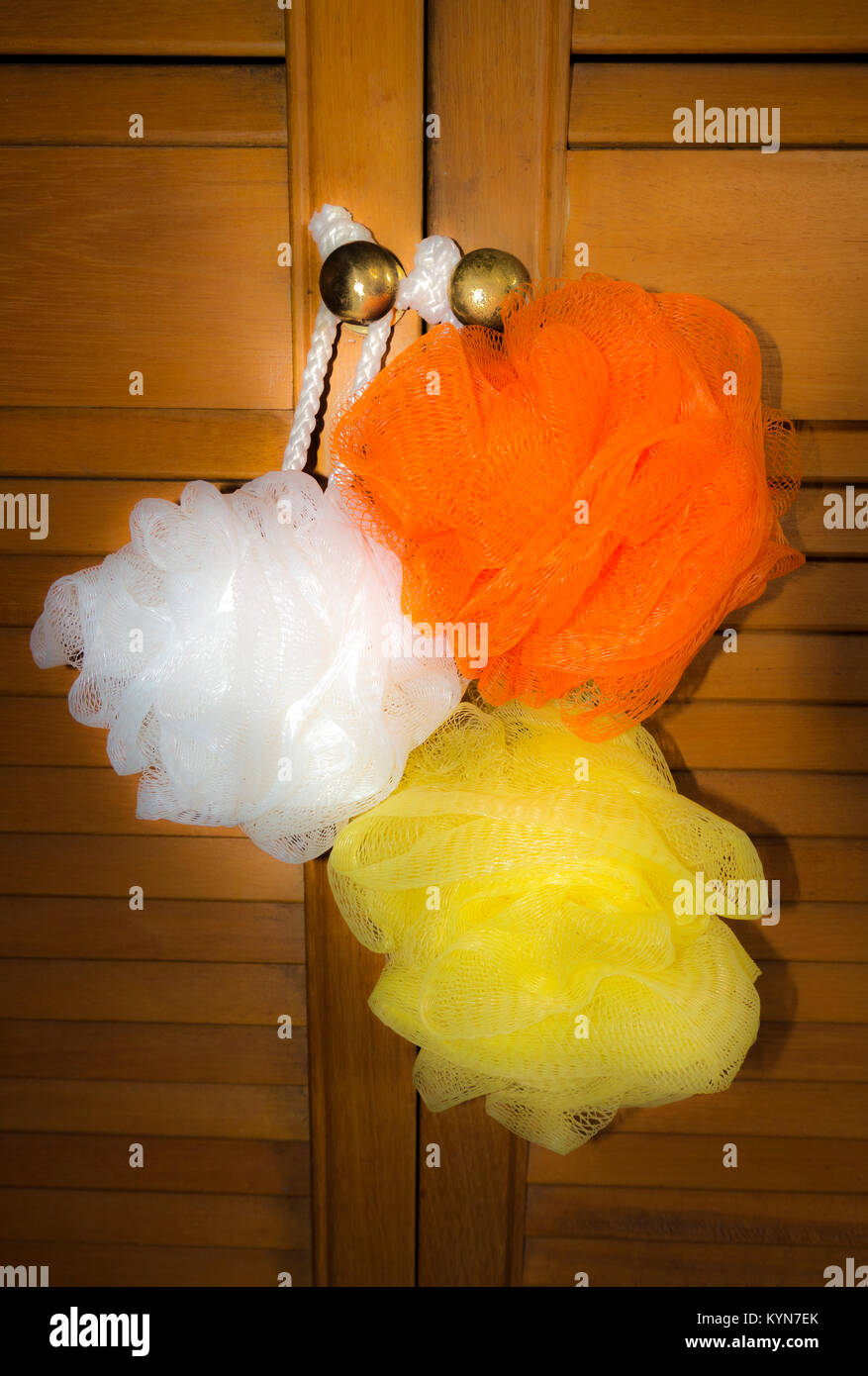 Three white, orange and yellow shower / bath scrunchies (polythene mesh exfoliating sponges), hanging on the knobs of louvred bathroom doors. Stock Photo