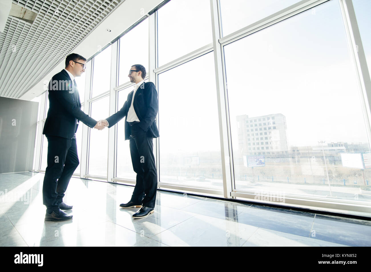 Full length side view of businessmen shaking hands in office building ...