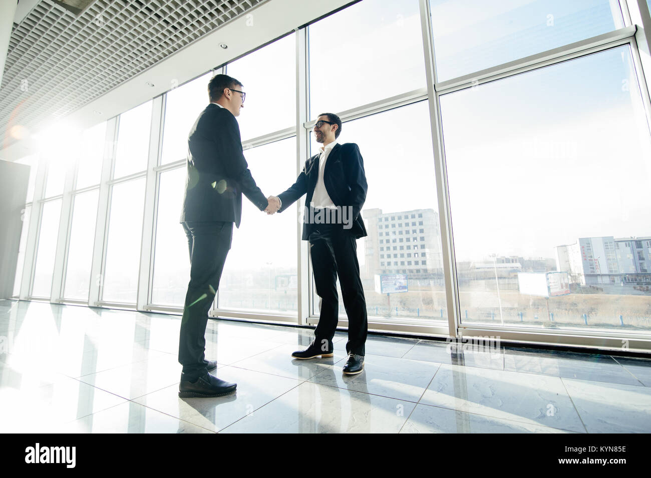 Full length side view of businessmen shaking hands in office building ...