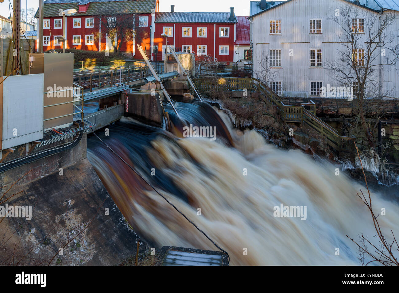Open flood gates at the city waterfall In Ronneby, Sweden. Flooding upstream makes the water overflow. Houses in background. Stock Photo