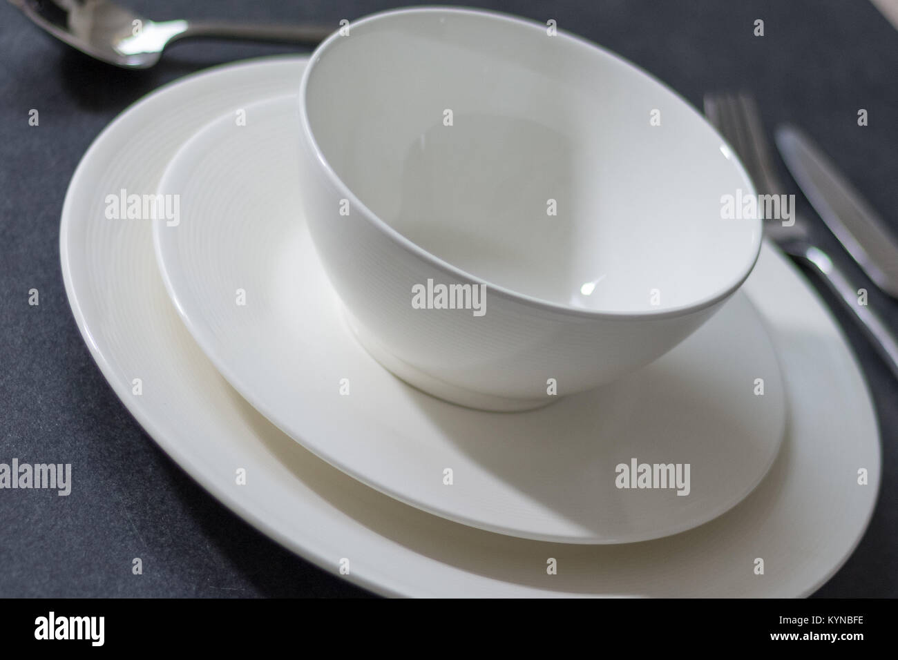Table setting with dinner plate empty round white plate on dark background with cutlery Stock Photo