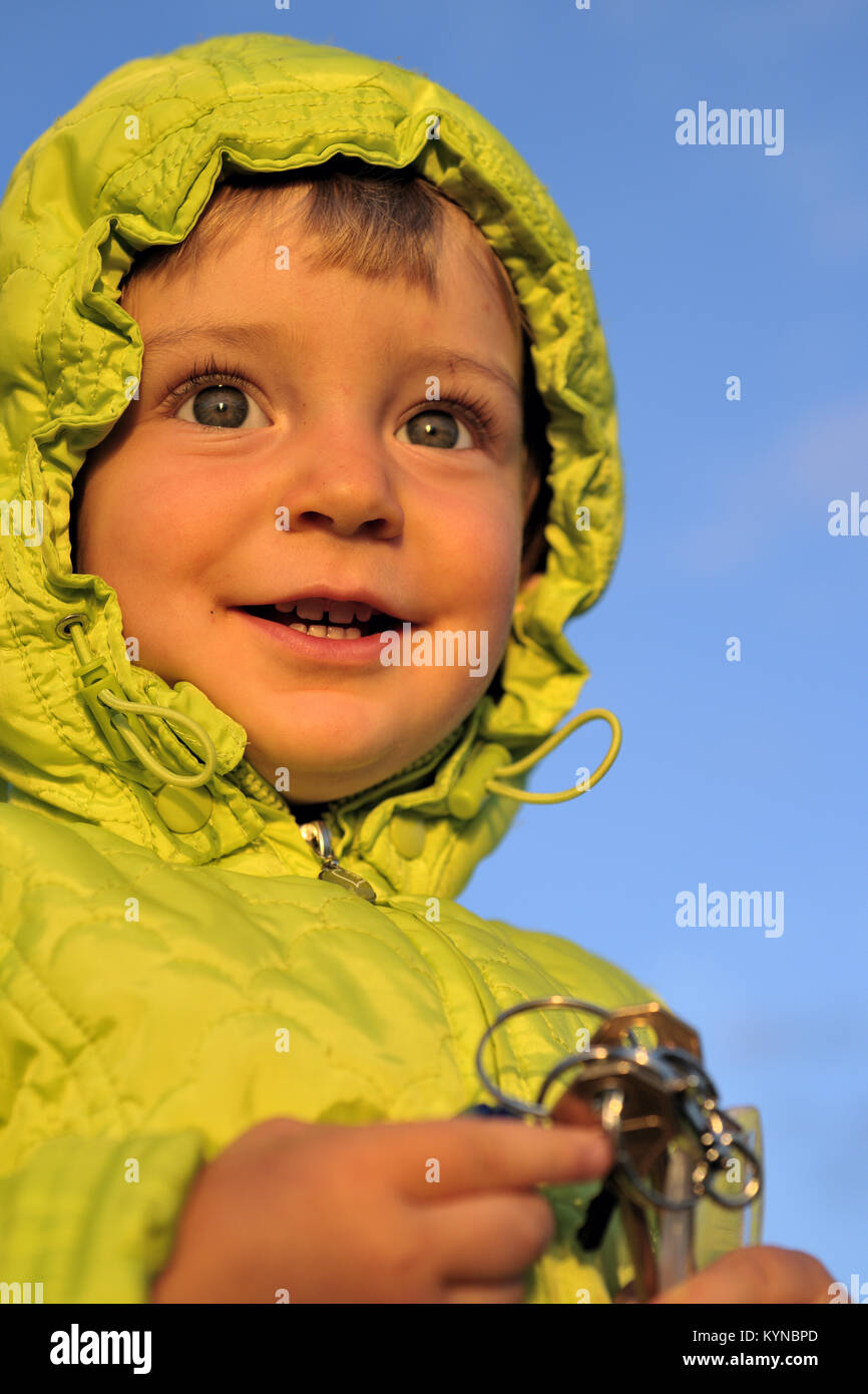 Portrait of little girl child with keys in sunny autumn evening, sunset sunlight. On the clear blue sky background Stock Photo