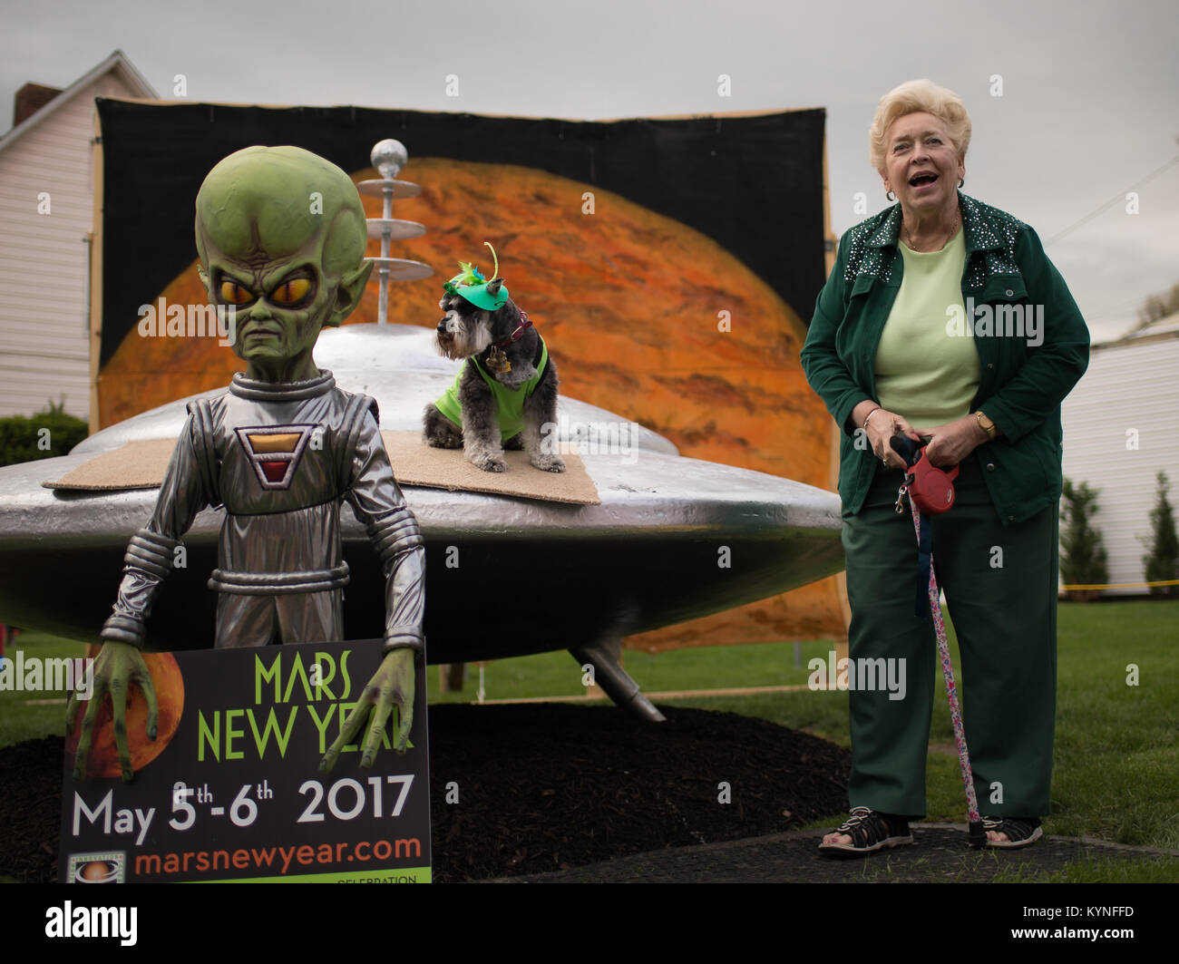 Sue Morris and her dog &quot;Pepper&quot; are seen with a model of a spacecraft and alien used for photos during the Mars New Year celebration Friday, May 5, 2017, in Mars, Pennsylvania. The town is hosting two days of Science, Technology, Engineering, Arts and Mathematics (STEAM) activities. Photo Credit: (NASA/Bill Ingalls) Stock Photo