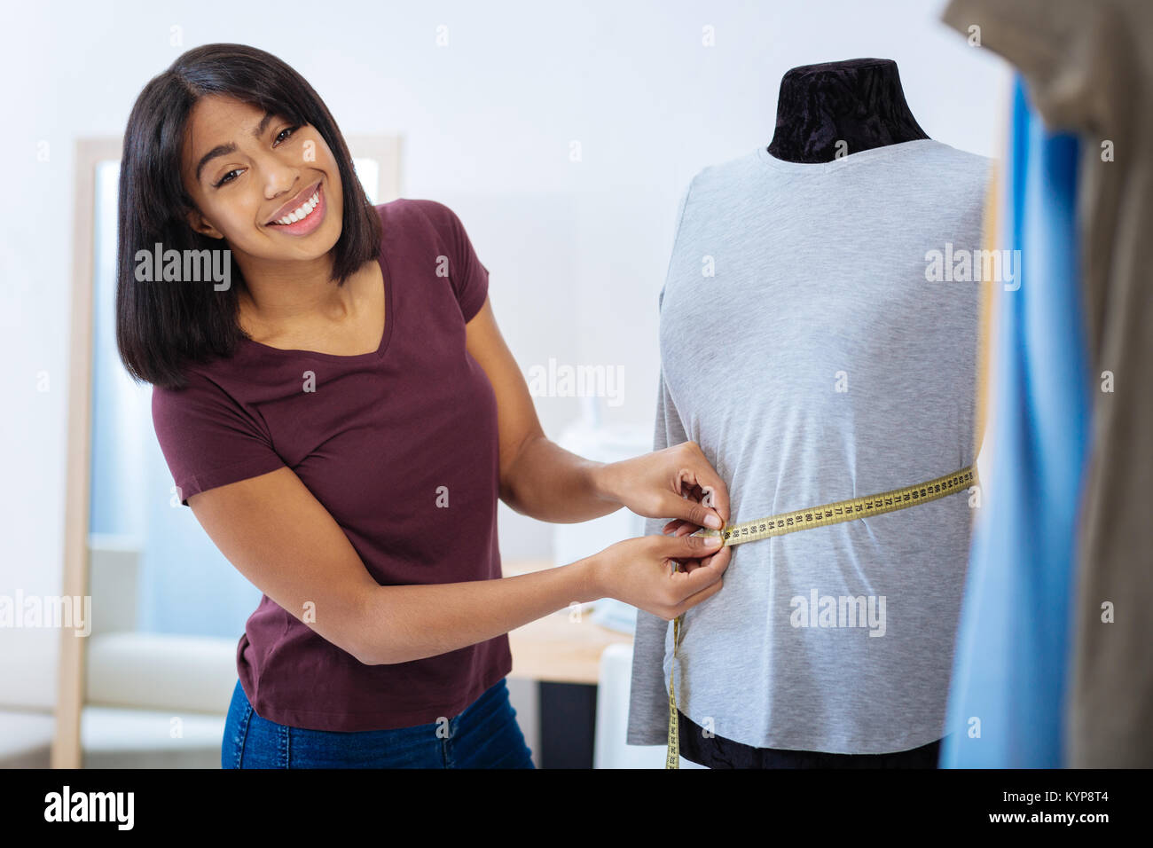 Smiling tailor feeling glad while measuring the mannequin Stock Photo