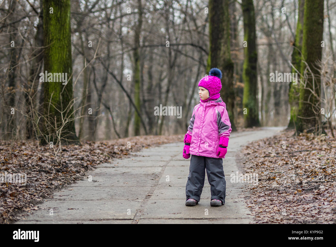 Little cute caucasian girl in a warm suit and knitted pink hat walking ...