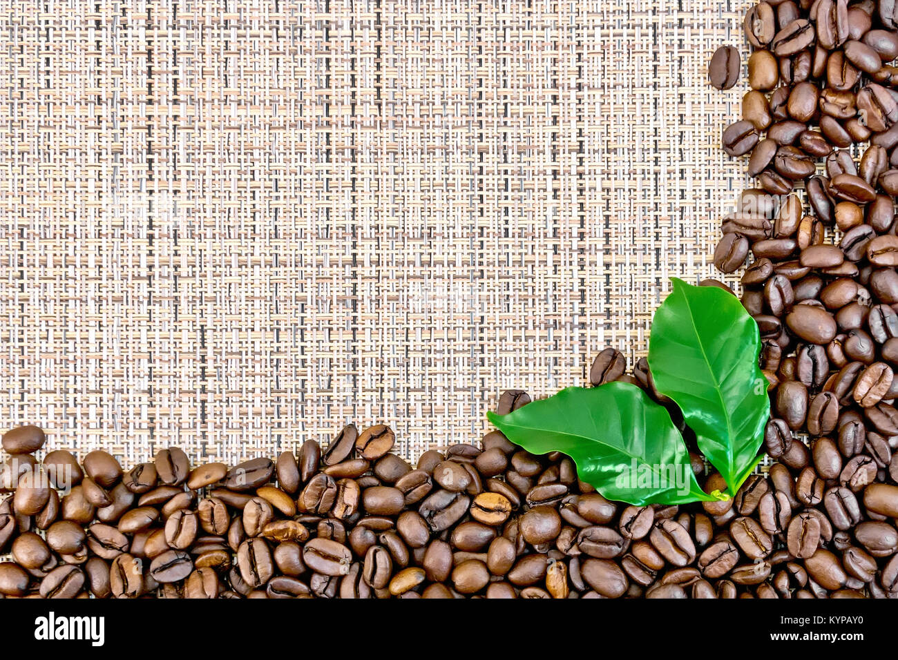 Frame of black coffee beans with leaves on brown coarse woven fabric Stock Photo