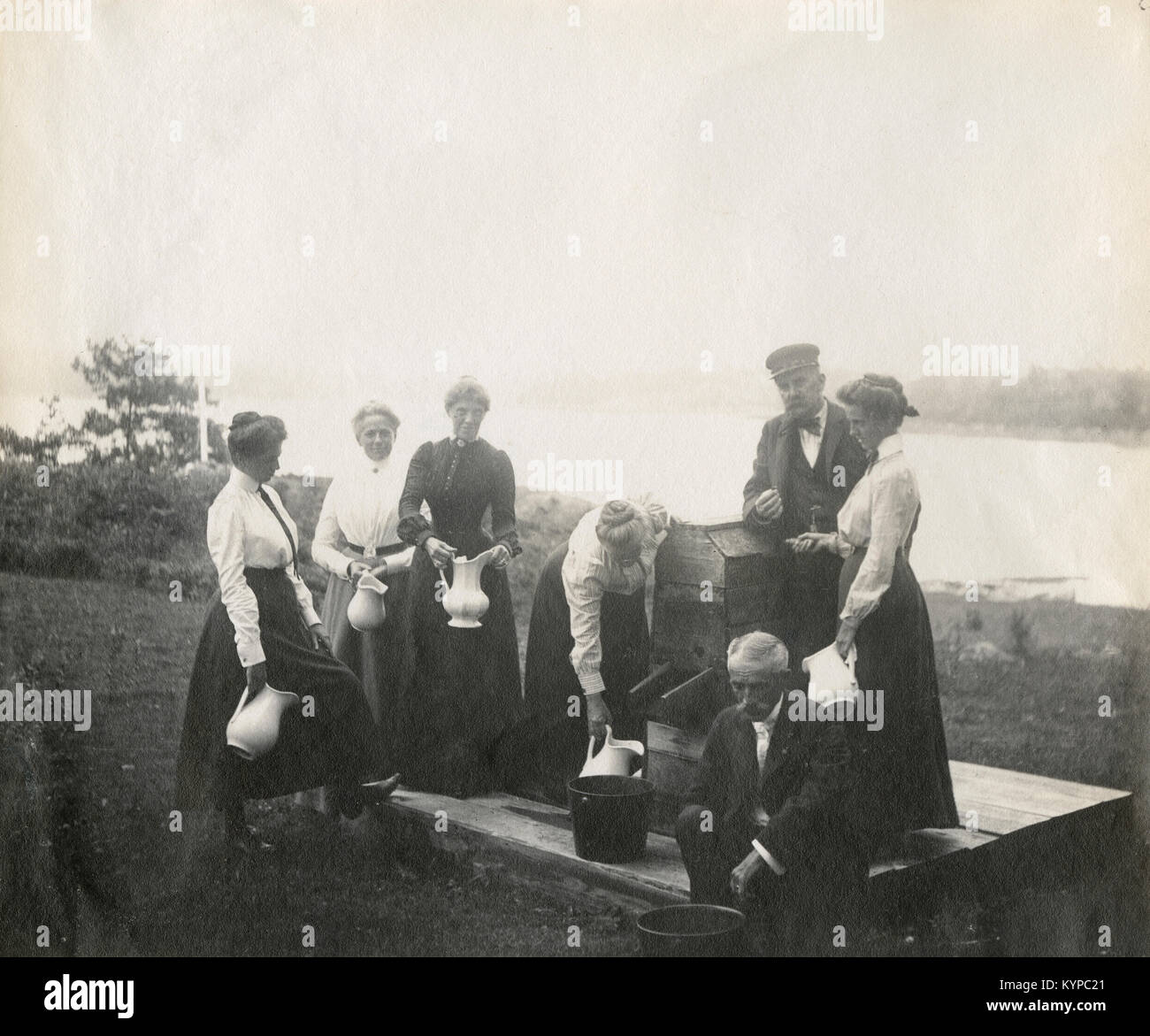 Antique circa 1905 photograph, family at water pump with river in background. Location is in or near Riggsville (now Robinhood), Maine in Sagadahoc County, USA. Stock Photo