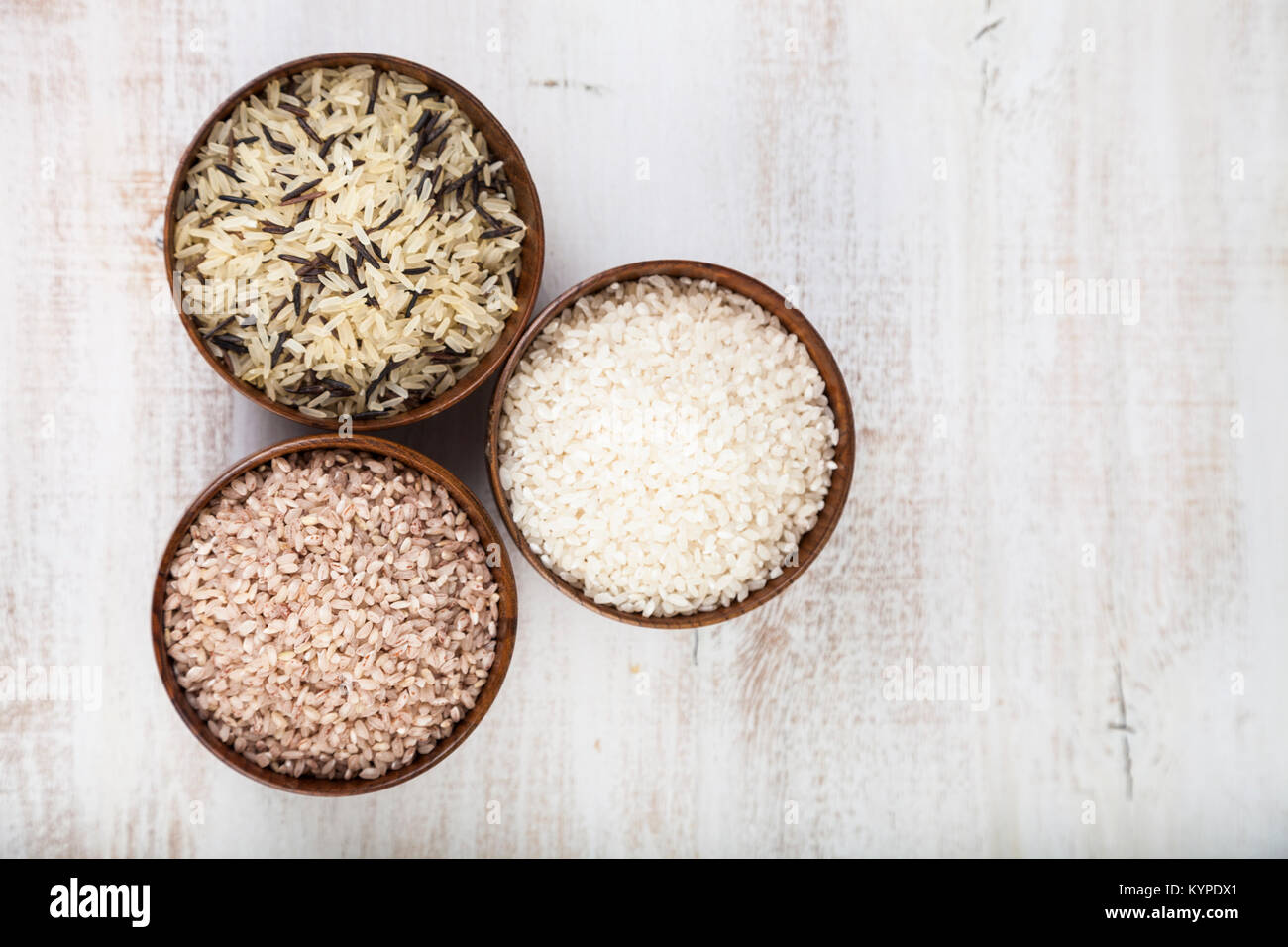 Three bowls with different varieties of rice on a wooden background ...