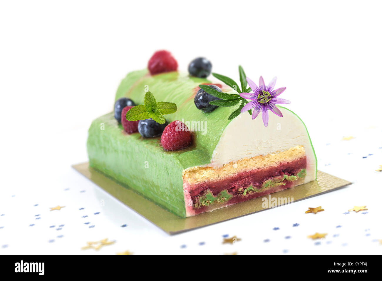 Pistachio Raspberry Yule Log decorated with fresh raspberries, blueberry, and pasion flower on white background. Stock Photo