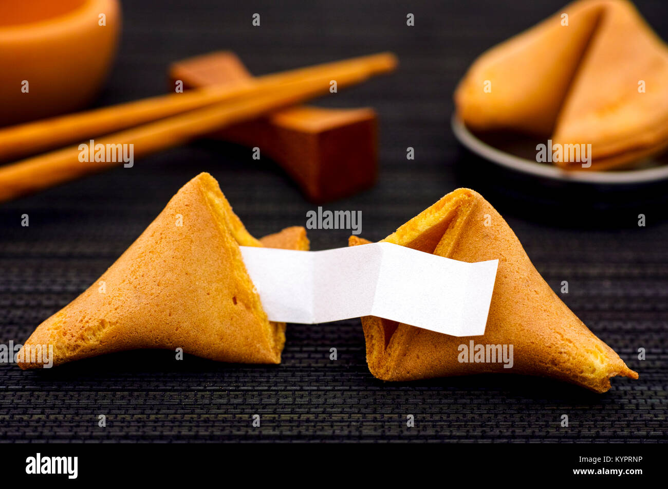 Fortune cookie with clear blank paper strip, another cookie and chopsticks on black napkin background. Close-up. Stock Photo