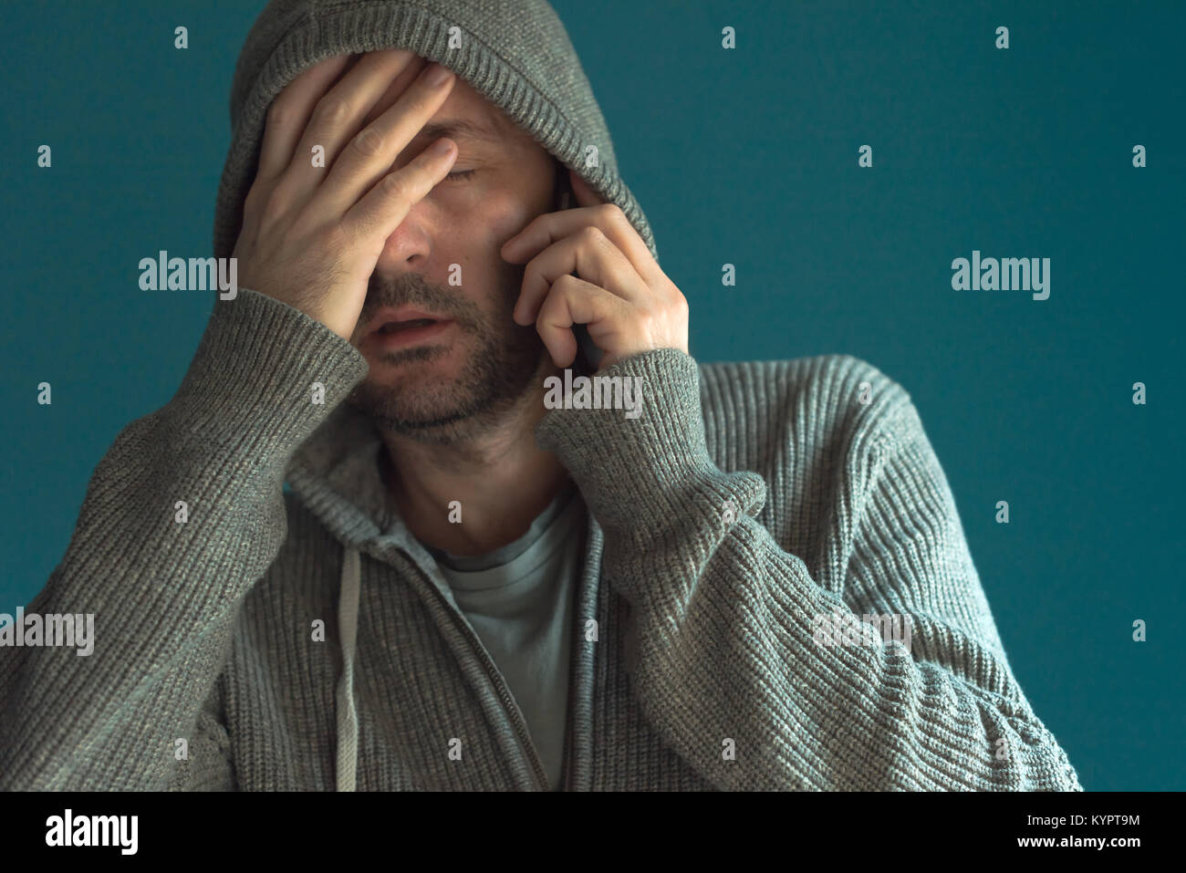 Face palm and mobile phone, man with hooded jacket covering face in disbelief while communicating over smartphone Stock Photo