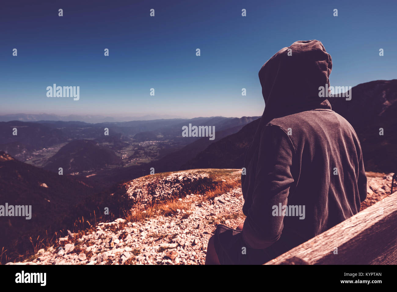 Mountain hiker at high viewpoint looking at the valley. Female tourist person in hooded jacket at mountain top enjoying the view,  ultra violet toned  Stock Photo