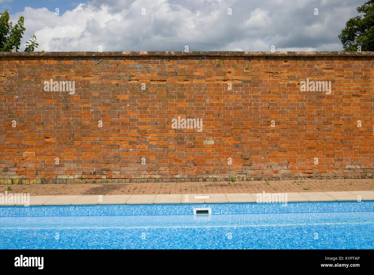 Old red brick wall contrasting with blue sky and swimming pool Stock Photo