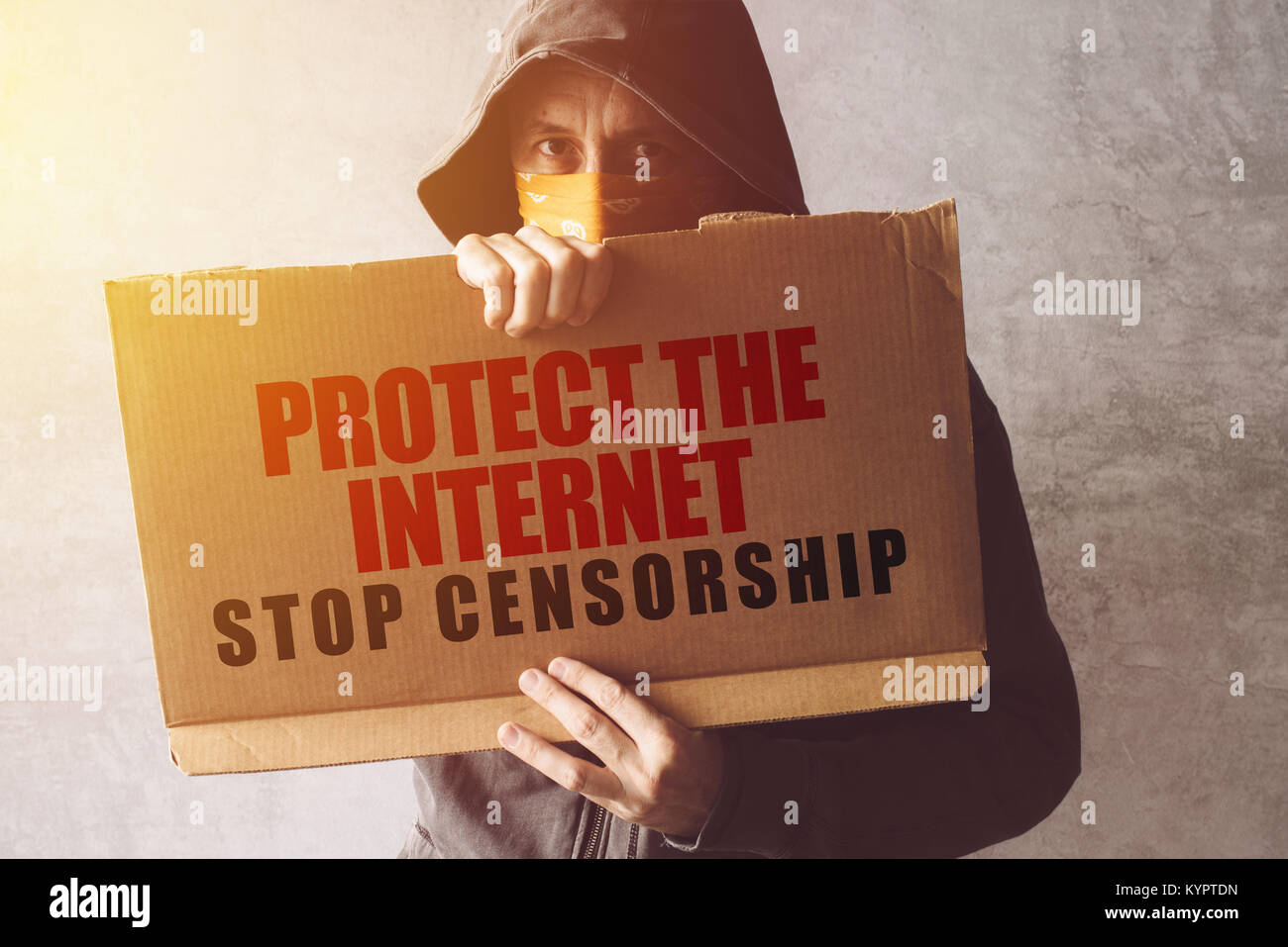 Hooded activist protestor holding Protect the Internet, stop censorship protest sign. Man with hoodie and scarf over face taking part in activism and  Stock Photo