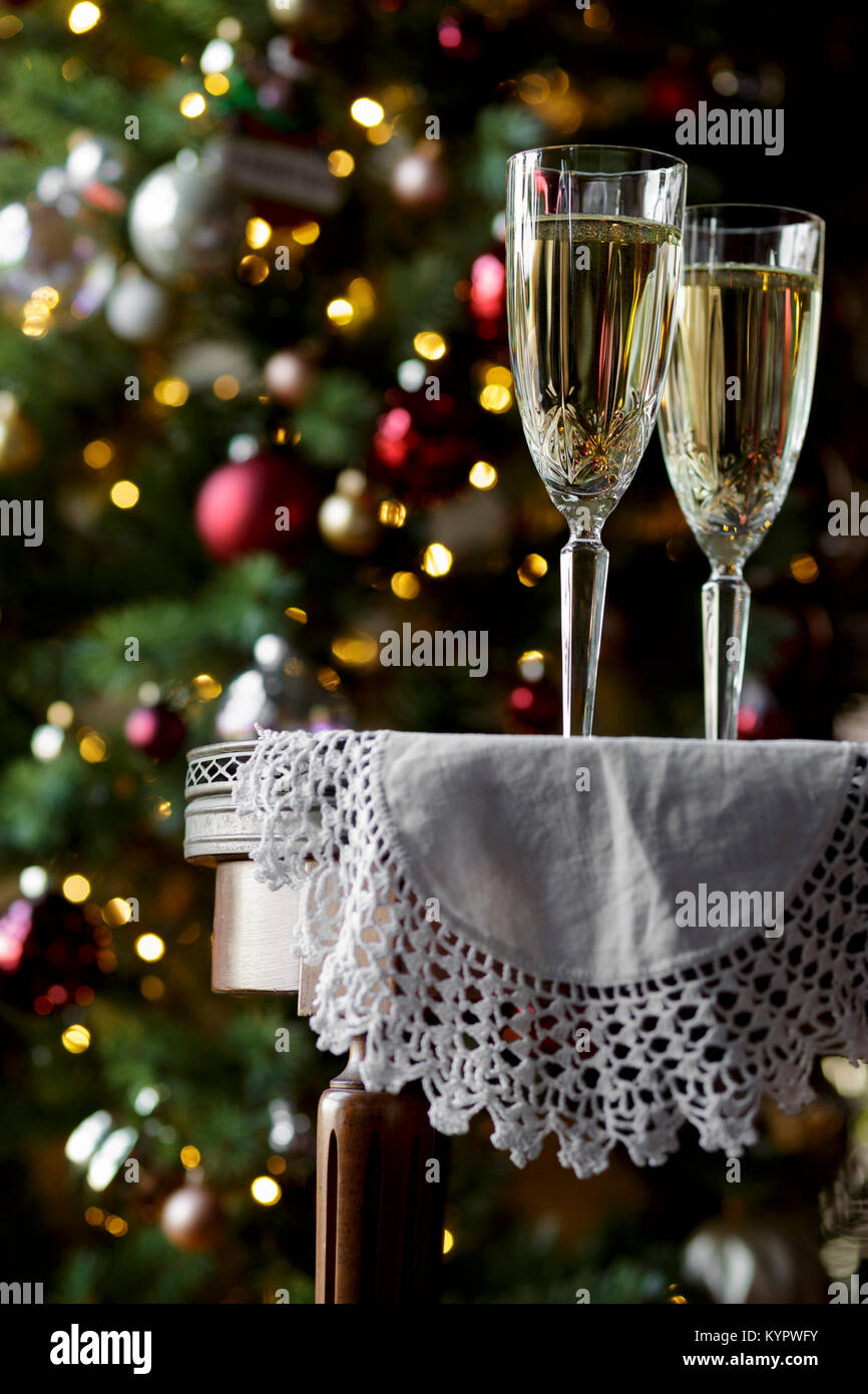 Champagne flutes on a table, with a Christmas tree behind Stock Photo