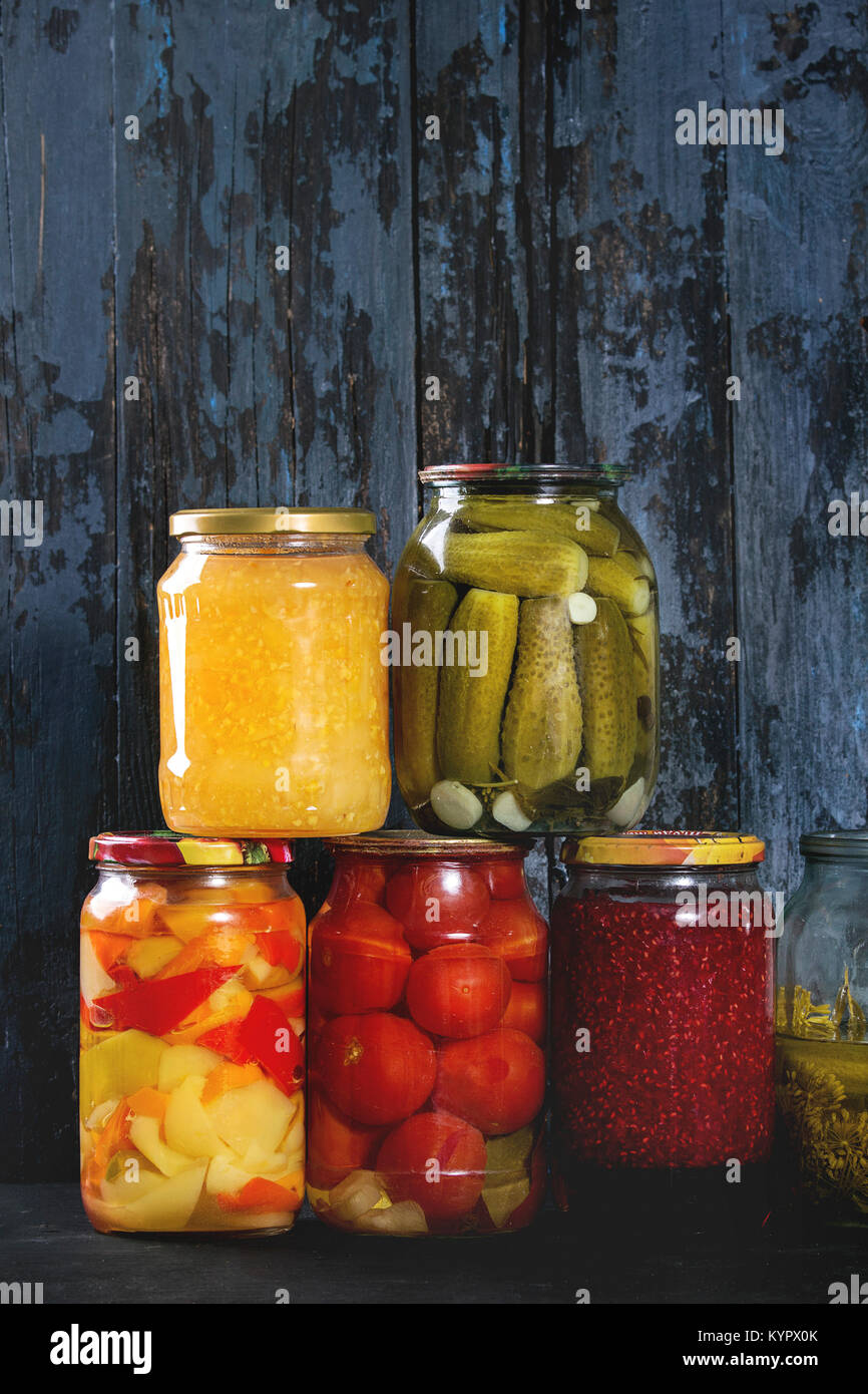 Variety glass jars of homemade pickled or fermented vegetables and jams in row with old dark blue wooden plank background. Seasonal preserves. Stock Photo