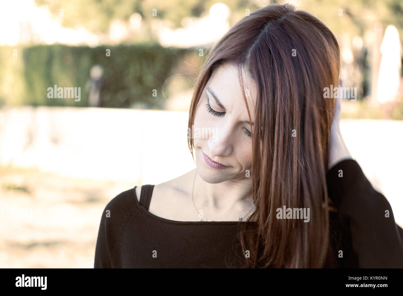 Portrait of a woman outdoors with her hand behind her head and looking down, worry, thinking. Stock Photo