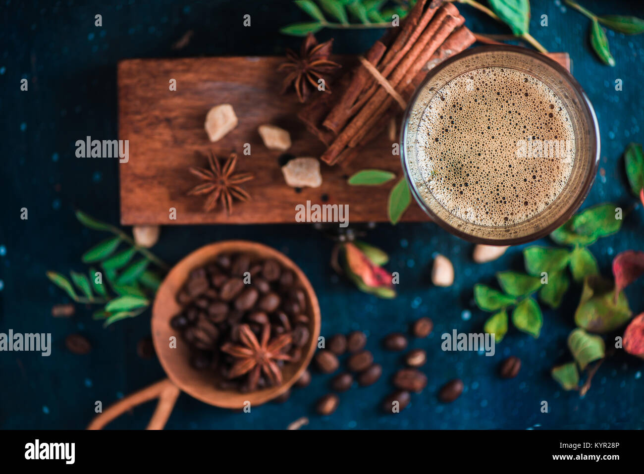 Close-up of espresso shot with foam on a wooden box, coffee beans, arabica leaves, cinnamon and spices on dark background. Hot drink photography conce Stock Photo