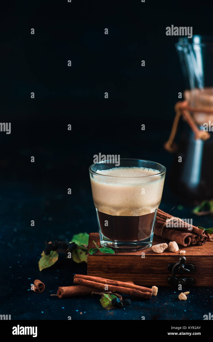 Espresso shot with foam on a wooden box with coffee beans, arabica leaves, cinnamon and spices