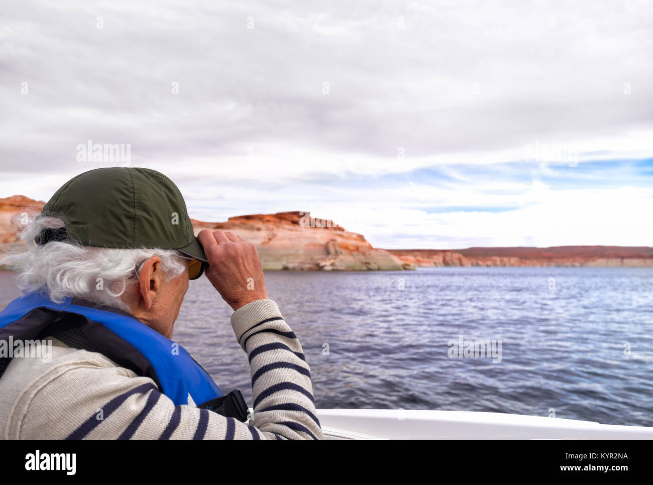 Active senior on a speedboat, holding onto his hat. He's wearing a discrete hearing aid, seen slightly behind his ear. Location: Lake Powell, Arizona Stock Photo