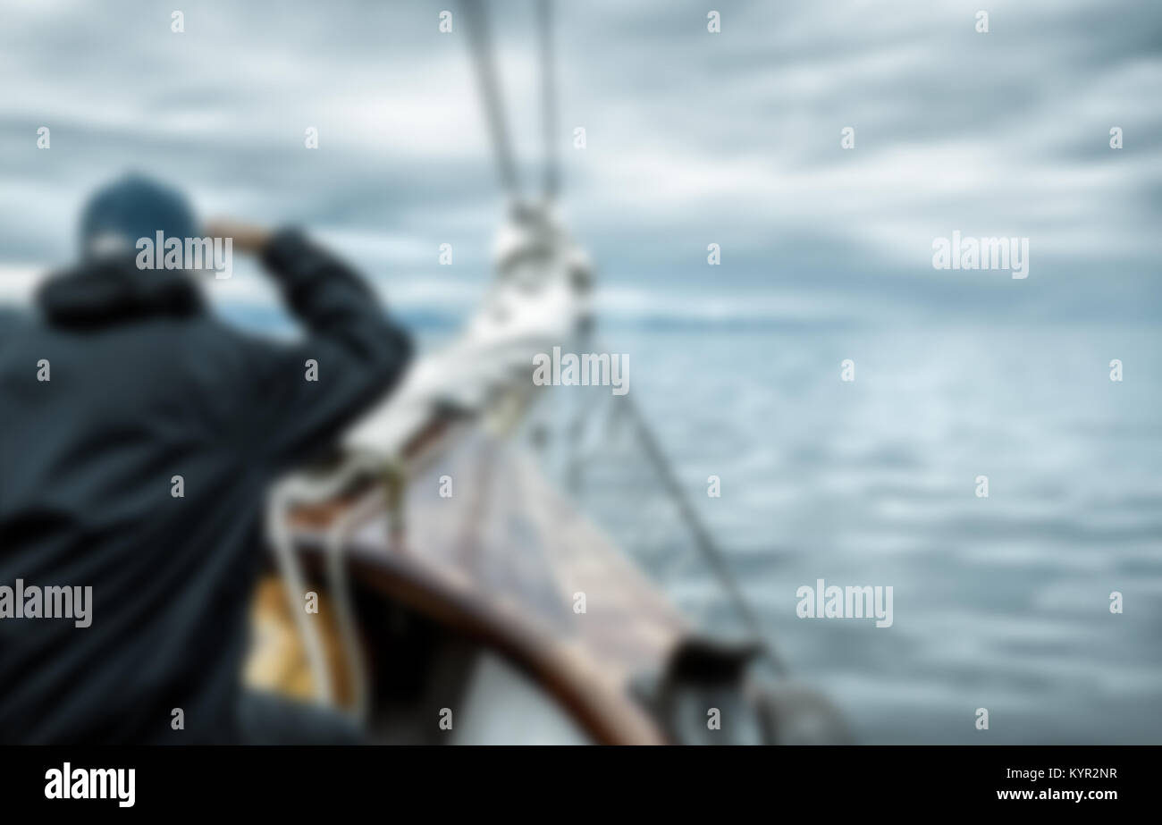 Sailing. Man leans off the front of the boat to scan the stormy horizon, on lookout duty for any obstacles or hazards. Blurred with copy space. Stock Photo